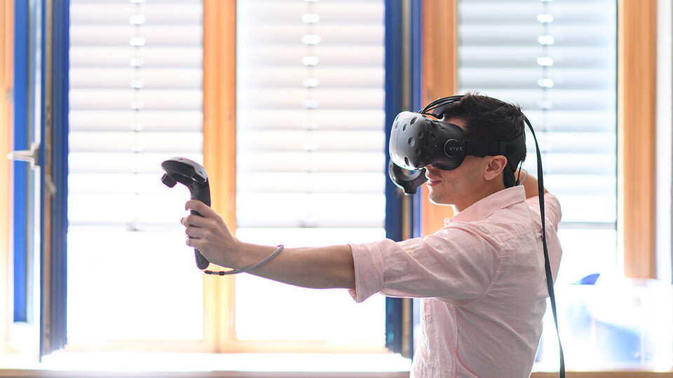 Eine Person trägt ein rosa farbenes Hemd und trägt eine VR Brille.