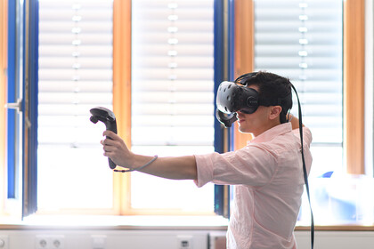 Eine Person trägt ein rosa farbenes Hemd und trägt eine VR Brille.