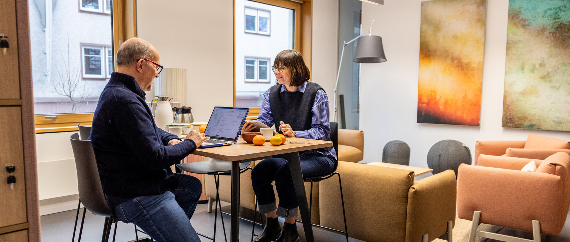 Ein mann und eine Frau sitzen sich gegenüber auf hohen Stühlen. Er arbeitete an einem Laptop