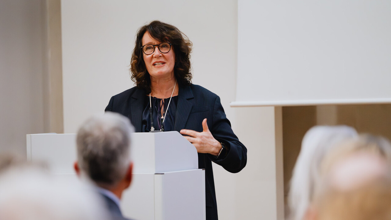 Das Bild zeigt die Festrednerin Caren Sureth-Sloane am Rednerpult. Im Vordergrund sieht man den verschommenen Hinterkopf des Rektors der Universität Mannheim