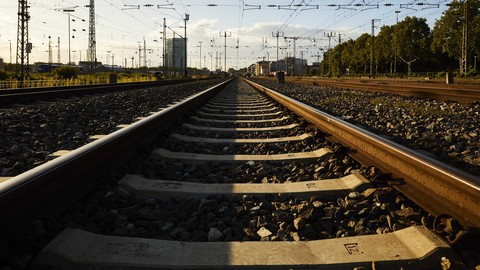 Blick auf eine Zugschiene im Abendlicht. Im Hintergrund sind ein paar Hochhausgebäude des Mannheimer Bahnhof erkennbar.