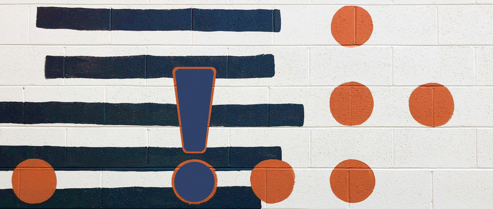 Eine Betonwand mit dunkelblauen Streifen, orangenen Punkten und einem großen Ausrufezeichen aufgemalt.