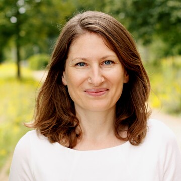 Corinna Braun hat braune schulterlange Haare. Sie trägt ein weißes Oberteil.