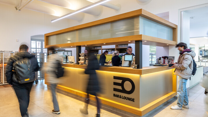 Ein Student bestellt etwas an der Theke der EO Bar&Lounge. Weitere Studierende laufen an der Theke vorbei.