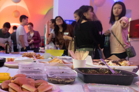 Auf einem Tisch stehen viele verschiedene internationale Speisen. Viele Menschen schauen vergnügt auf das Essen.