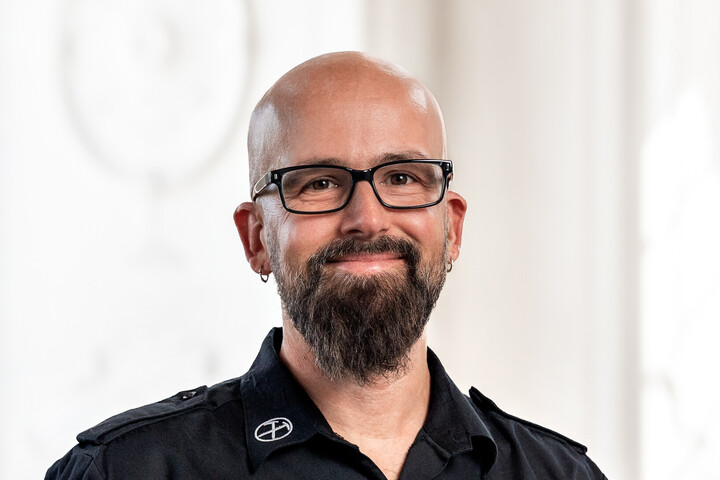 Prof. Dr. Heiko Paulheim trägt eine dunkle Brille und ein dunkles Hemd, er hat eine Glatze, einen dunklen Bart und Ohrringe. 