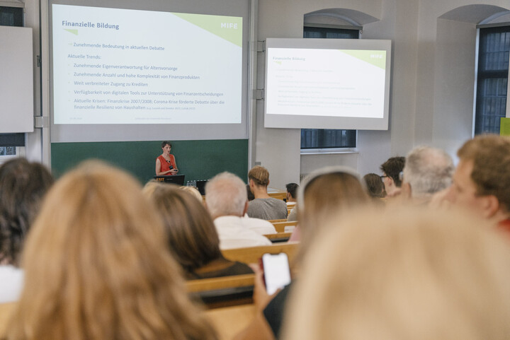 Eine Person steht vor einem Publikum und hält einen Vortrag.