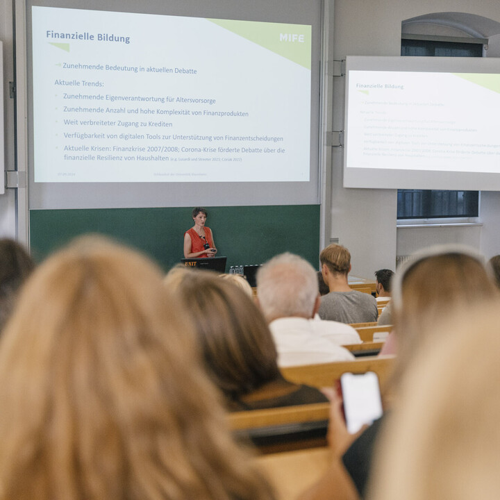 Eine Person steht vor einem Publikum und hält einen Vortrag.