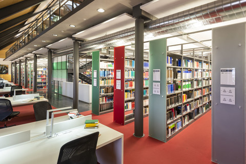 In der Ehrenhof-Bibliothek ist ein roter Teppichboden. Viele große Bücherregale stehen in der Mitte des Raumes, an der Seite sind Schreibtische. 