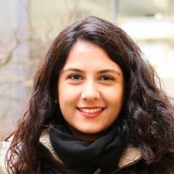 Ein Porträtfoto von Areso Ahmadi. Sie hat dunkelbraune, lockige Haare, trägt einen schwarzen Schal und lächelt.