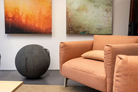 Das BIld zeigt einen erdtonfarbenen Sessel und einen stoffbezogenen grau-melierten Sitzball.