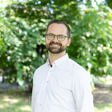  Lukas Dausend. Er lächelt freundlich, trägt ein weißes Hemd und eine Brille.