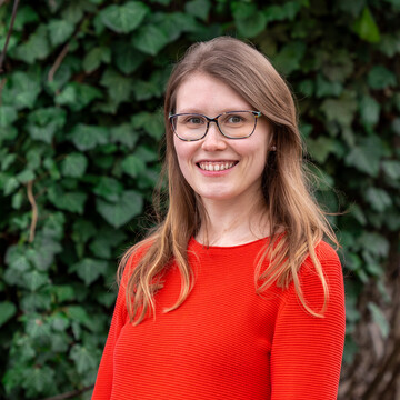 Julia Freimuth. Julia Freimuth lächelt breit und trägt ein rotes Oberteil und Brille.