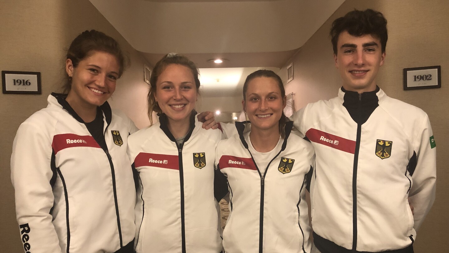 Vier Hockey-Spieler in Sportkleidung stehen nebeneinander und lächeln.