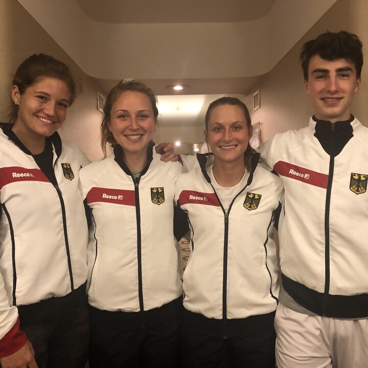 Vier Hockey-Spieler in Sportkleidung stehen nebeneinander und lächeln.
