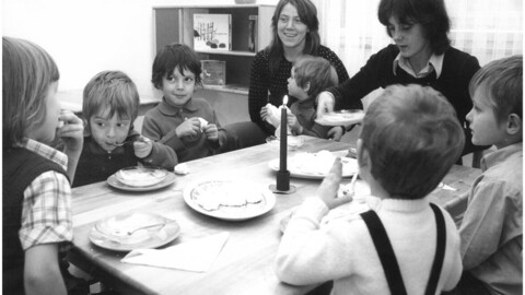 An einem Tisch sitzen acht Personen, wovon sechs Kinder sind. Einige der Kinder sind am Essen.