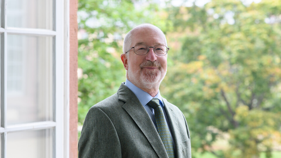 Portrait von Jochen Taupitz. Er trägt einen grünen Anzug und steht lächelnd vor einem Fenster.