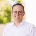 Eine lächelnde Person trägt ein weißes Hemd und steht vor einem grün verschwommenem Hintergrund. Die Person heißt Markus Strohmaier.