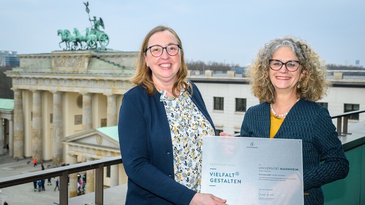 Alexandra Raquet und Sabine Kußmaul mit dem Zertifikat des Stifterverbandes in der Hand. Im Hintergrund ist das Brandenburger Tor in Berlin zu sehen.
