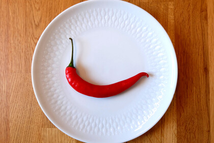 Eine rote Chilischote liegt auf einem weißen Teller.