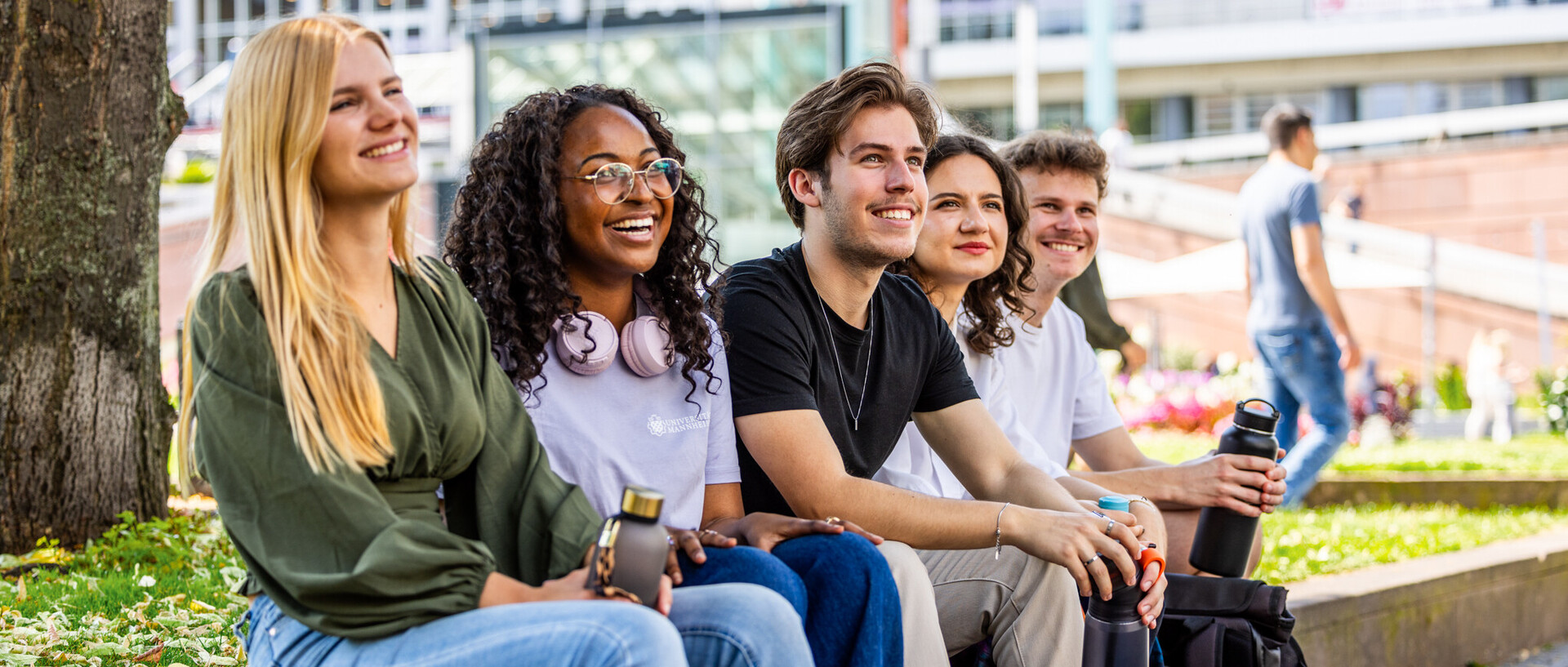 Eine Gruppe gut gelaunter Studierende sitzt an einem sonnigen Tag am Paradeplatz. Alle lachen und scheinen glücklich zu sein.