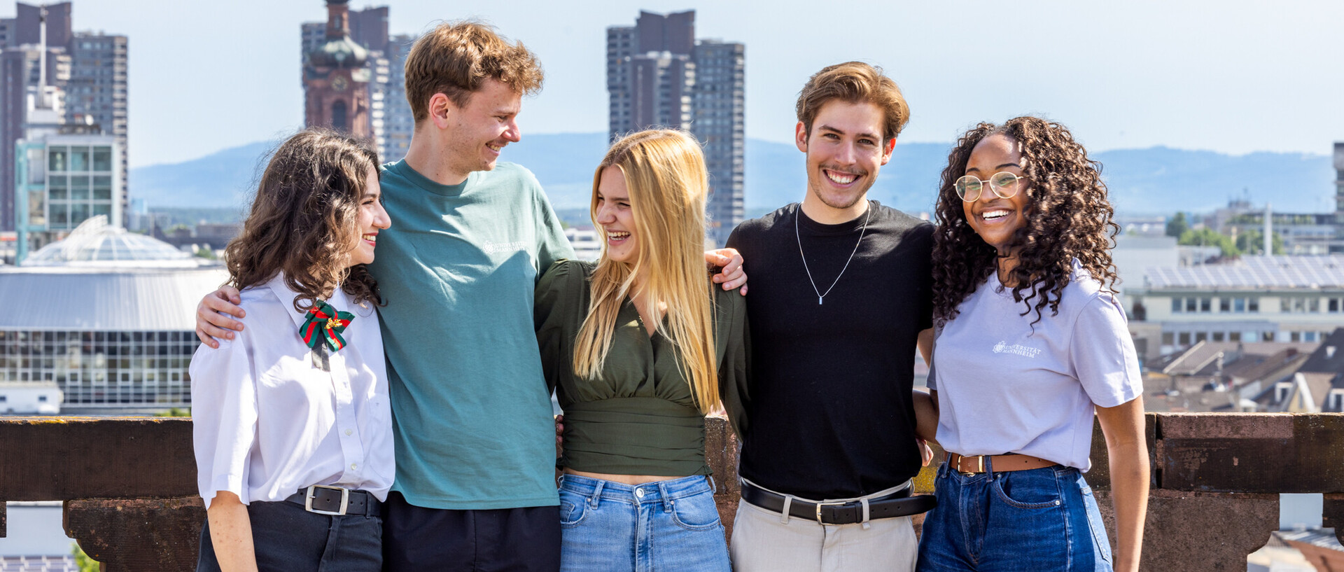 Eine Gruppe von fünf Studierenden auf dem Schlossdach. Sie halten sich gegenseitig im Arm, lachen und scheinen gute Laune zu haben.