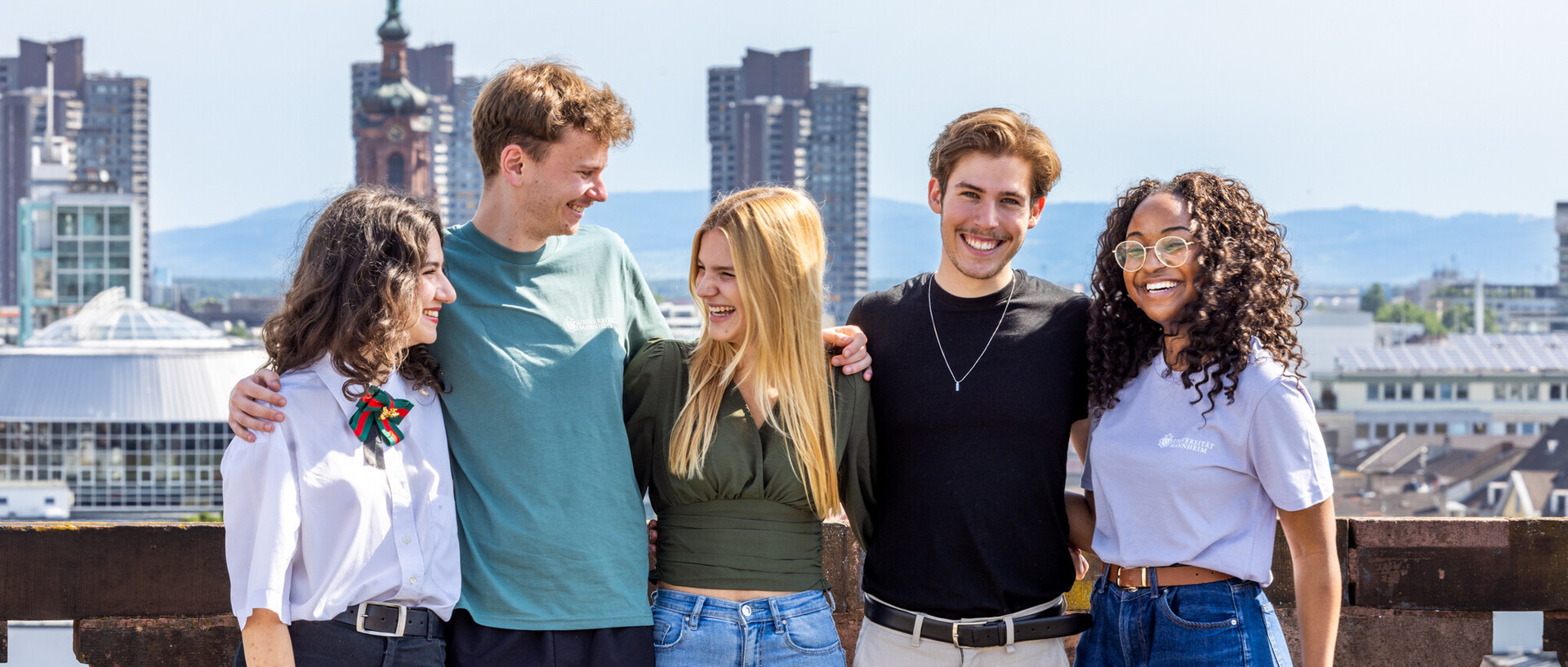 Eine Gruppe von fünf Studierenden auf dem Schlossdach. Sie halten sich gegenseitig im Arm, lachen und scheinen gute Laune zu haben.