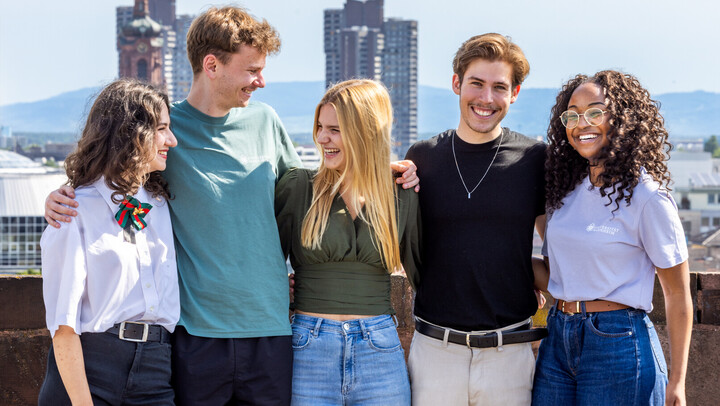 Eine Gruppe von fünf Studierenden auf dem Schlossdach. Sie halten sich gegenseitig im Arm, lachen und scheinen gute Laune zu haben.