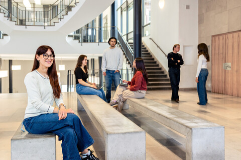 Eine Studentin sitzt auf einer Seitenbank im Ostflügel des Schlosses. Im Hintergund unterhalten sich weitere Studierende. 