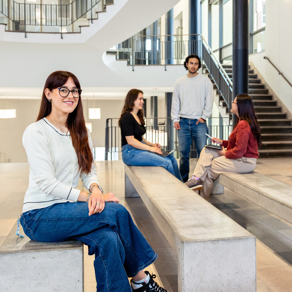 Eine Studentin sitzt auf einer Seitenbank im Ostflügel des Schlosses. Im Hintergund unterhalten sich weitere Studierende. 