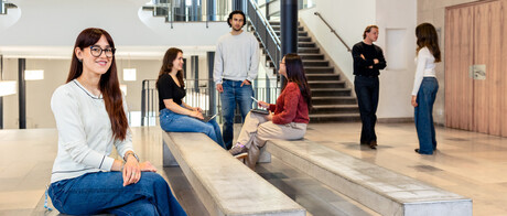 Eine Studentin sitzt auf einer Seitenbank im Ostflügel des Schlosses. Im Hintergund unterhalten sich weitere Studierende. 