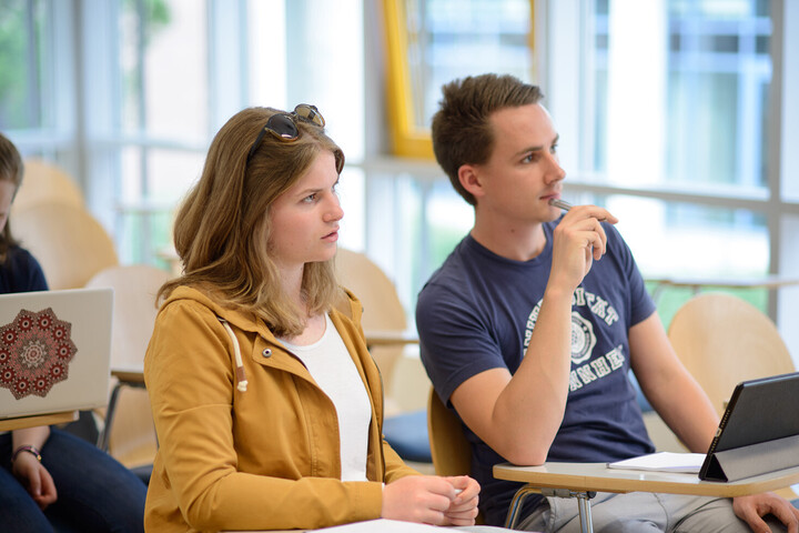Zwei Studierende hören interessiert bei einer Vorlesung zu.