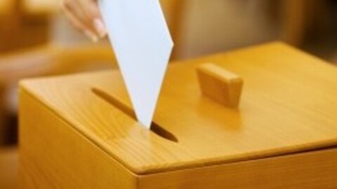 Eine Person wirft einen weißen Umschlag in eine Wahlurne.