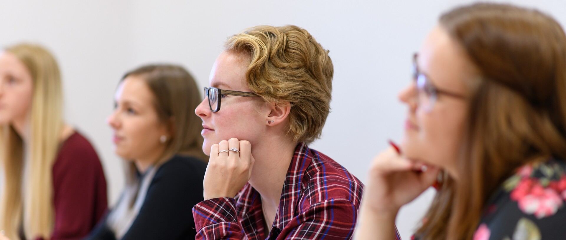 Studierende sitzen an einem Tisch und hören bei einem Vortrag zu.