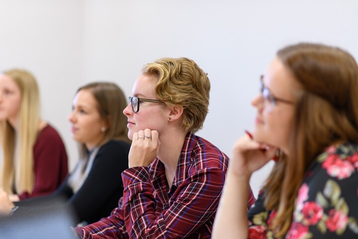 Studierende sitzen an einem Tisch und hören bei einem Vortrag zu.