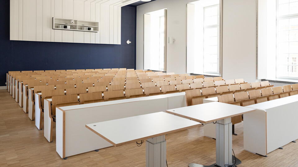 Weiße Reihentische und braune Klappstühle im Hörsaal EO 165.