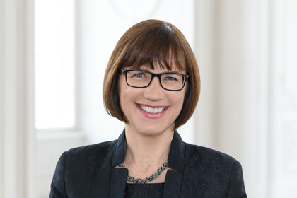 Frau Kehnel steht vor einem hellen Hintergrund und lächelt.