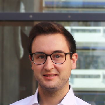 Adrian Rebmann hat kurze braune Haare. Er trägt eine dunkle Brille und ein lilanes Hemd.