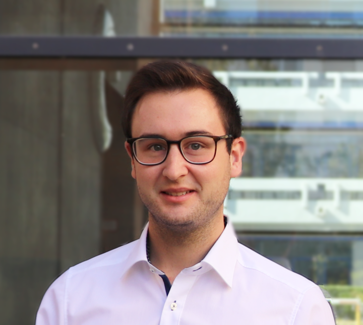 Adrian Rebmann hat kurze braune Haare. Er trägt eine dunkle Brille und ein lilanes Hemd.