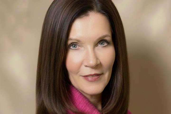 Alumna Dr. Iris Reinelt hat schulterlange, glatte braune Haare, trägt einen Rollkragenpullover in pink und lächelt.