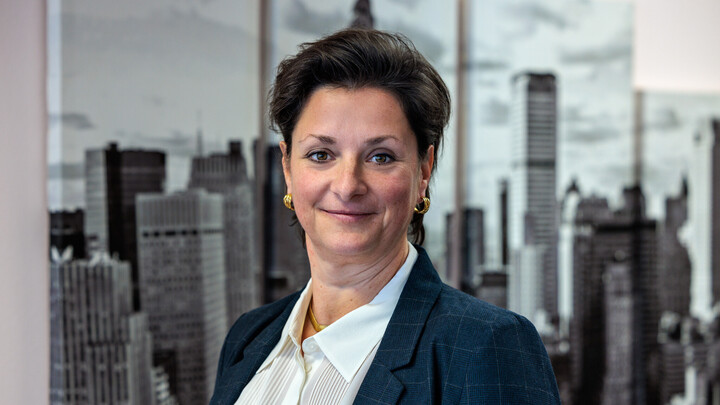 Portraitfoto von Prof. Dr. Stefanie Schäfer vor einem Bild einer Skyline. Sie trägt eine weiße Bluse und einen dunkelblauen Blazer. 