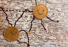 Zwei Geldmünzen liegen auf einer geographischen Karte. Mit einem schwarzen Stift wurden Arme und Beine an die Münzen angefügt und Gesichter auf die Münzen gemalt.