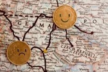 Zwei Geldmünzen liegen auf einer geographischen Karte. Mit einem schwarzen Stift wurden Arme und Beine an die Münzen angefügt und Gesichter auf die Münzen gemalt.