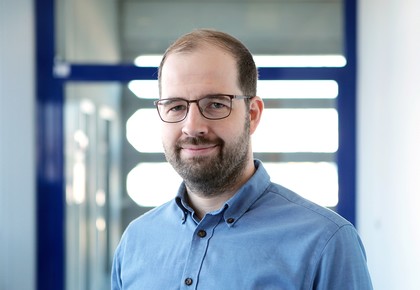 Dr. Lars Leszczensky hat einen Bart und kurze braune Haare. Er trägt ein blaues Hemd.