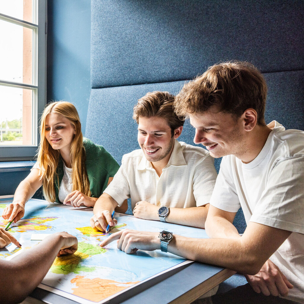Vier Studierende an einem Arbeitsgruppentisch. Sie schauen gemeinsam auf ein Dokument. 