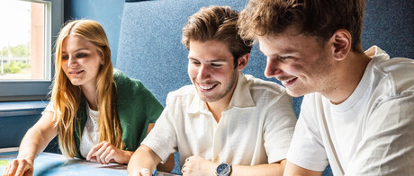 Vier Studierende an einem Arbeitsgruppentisch. Sie schauen gemeinsam auf ein Dokument. 