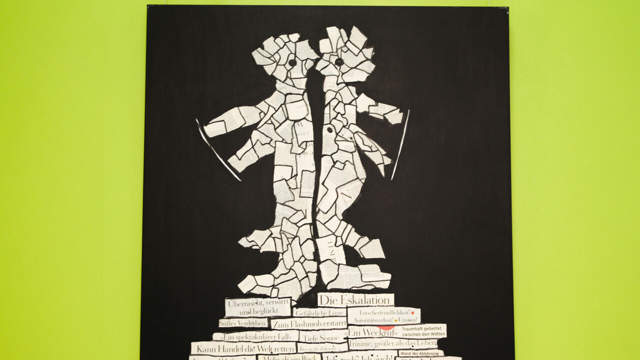 Vor einer grünen Wand hängt ein Kunstwerk. Abgebildet ist eine Zeitungscollage in Form von zwei Figuren vor schwarzem Hintergrund.