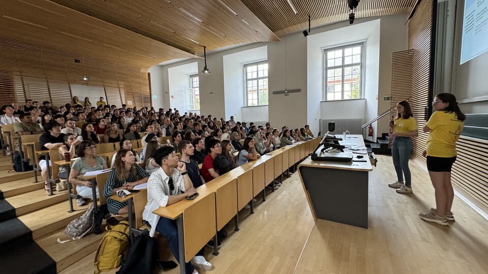 Studierende sitzen in einem Hörsaal und schauen auf die Powerpoint-Präsentation an der Wand.