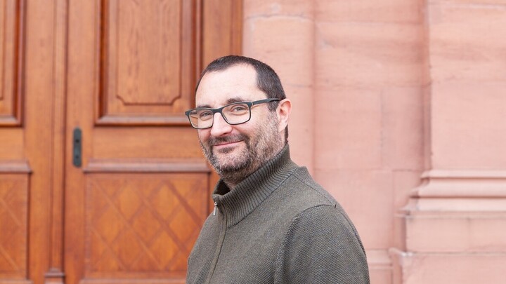 Helge Rückert trägt einen braunen Pullover und steht im ehrenhof des Mannheimer Schlosses.