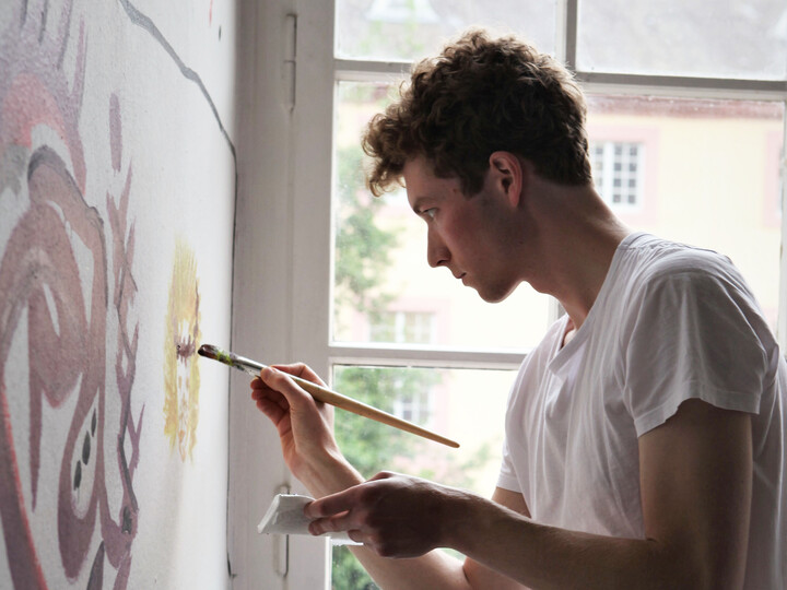 Ein junger Mann bemalt eine weiße Wand mit gelber Farbe